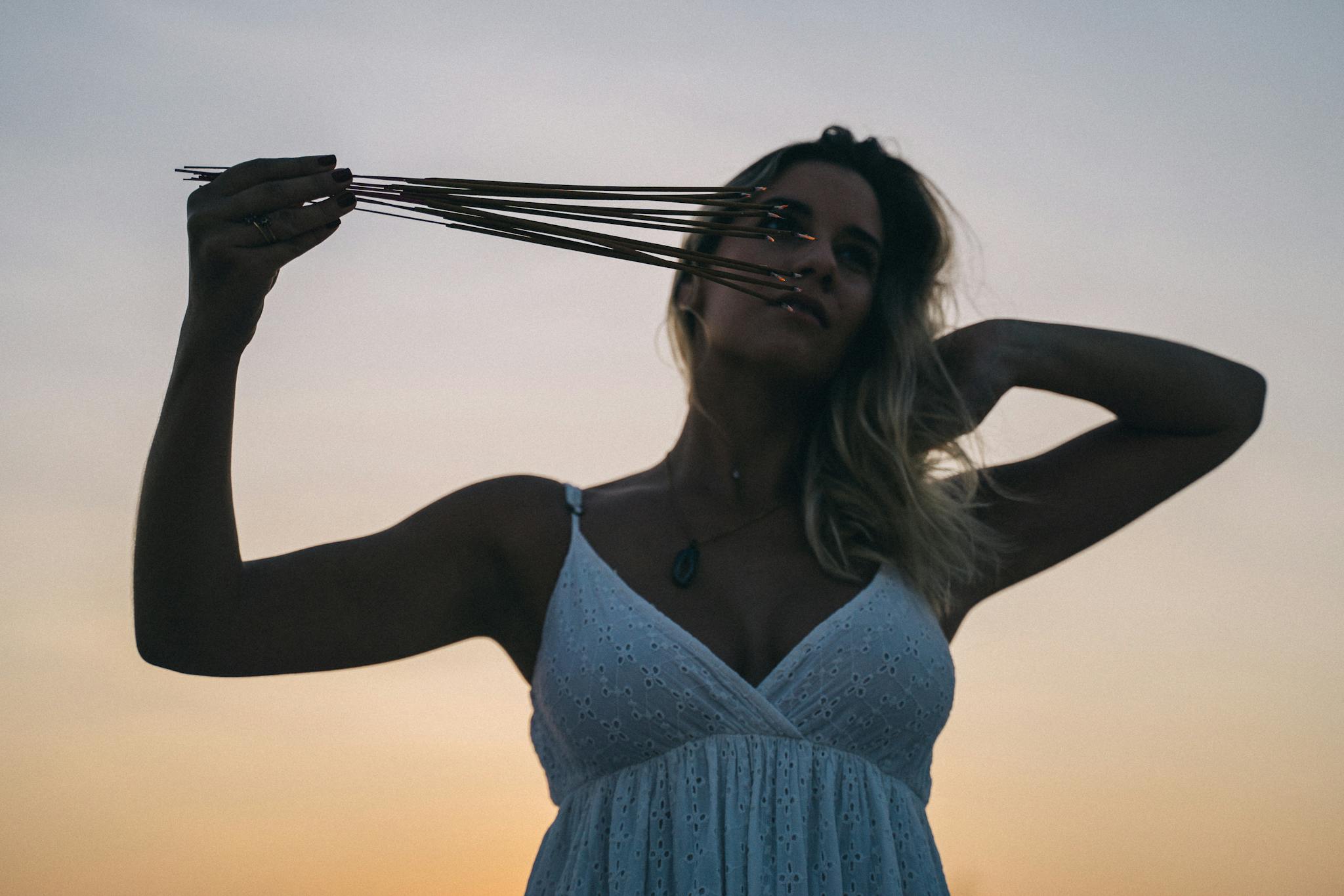 A woman holding incense sticks in a peaceful sunset setting, embracing calmness and spirituality.