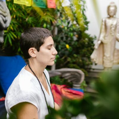 A person engaged in serene meditation outdoors near a Buddha statue amidst lush greenery.