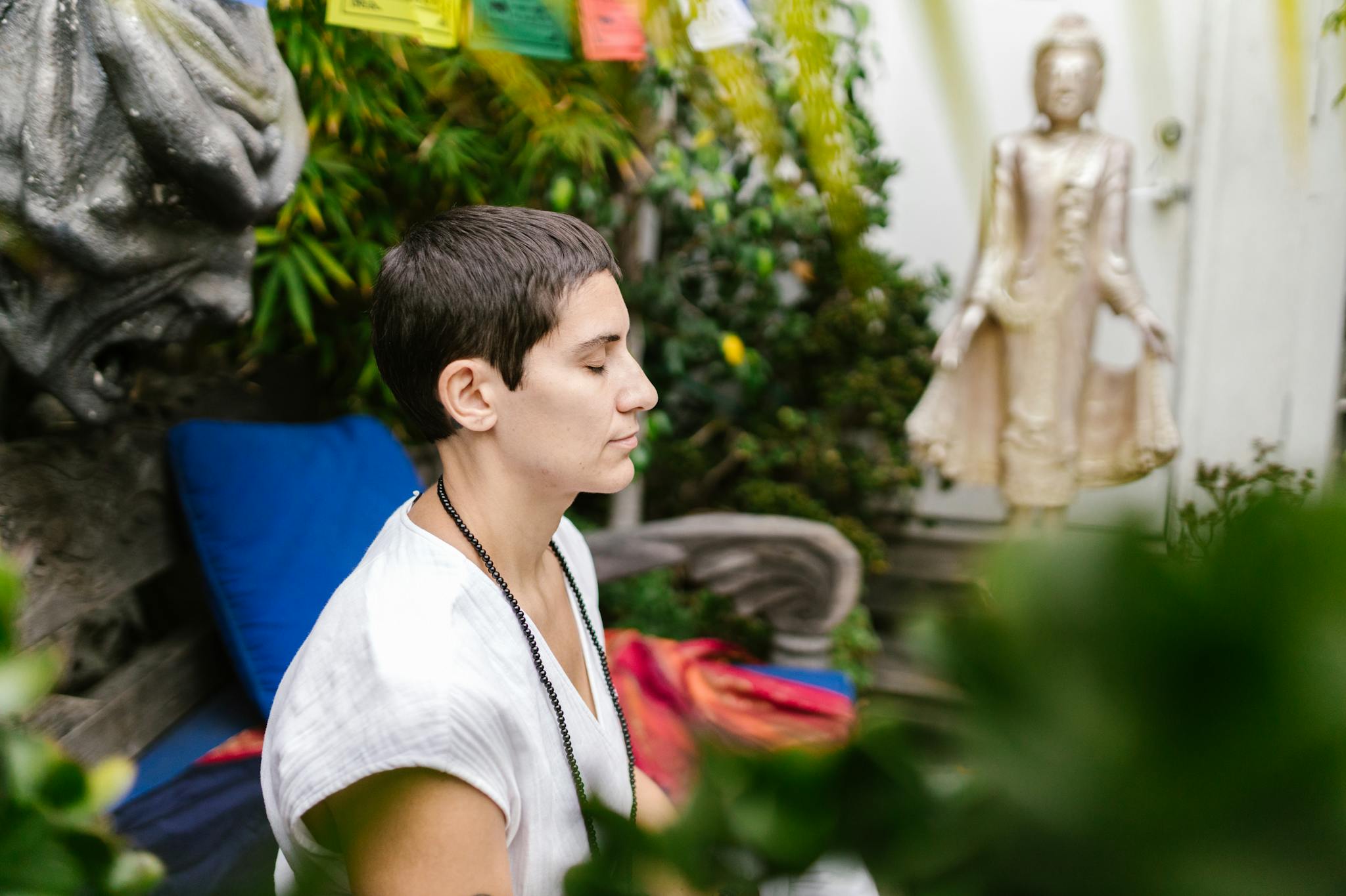 A person engaged in serene meditation outdoors near a Buddha statue amidst lush greenery.
