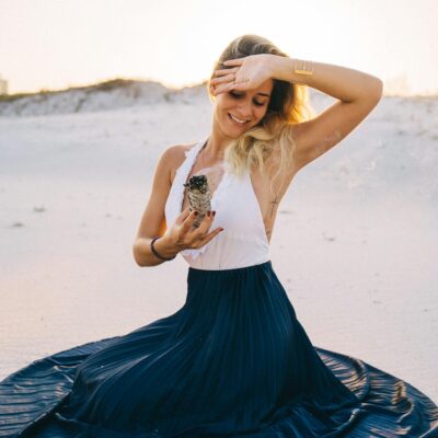 A serene woman meditating on a beach holding white sage, bathed in warm sunlight.